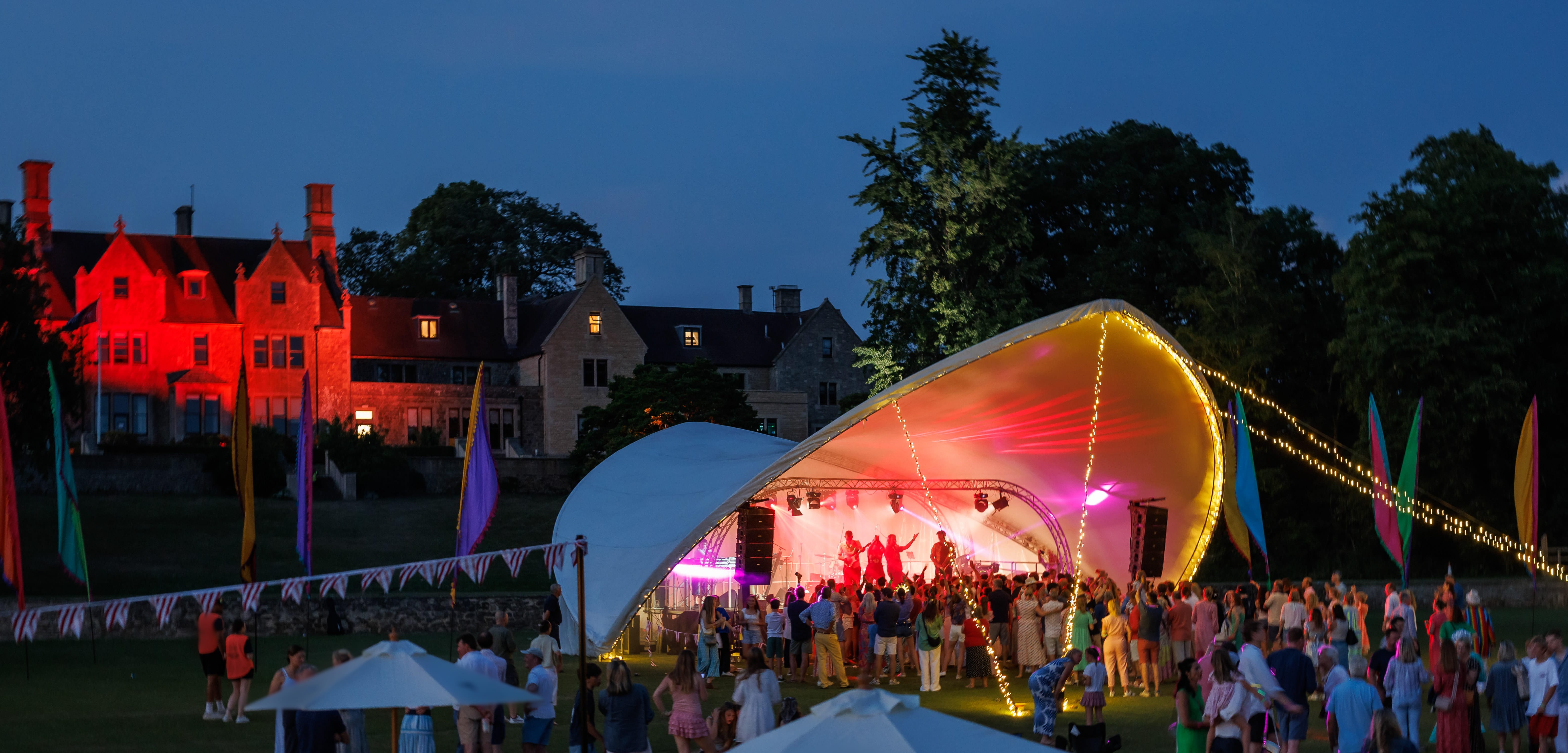 an outstanding school festival at night with people gathering around the stage with the school in the background
