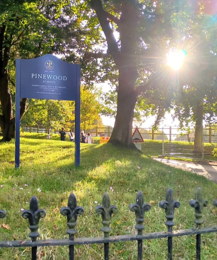 Pinewood School entrance with beautiful green trees and the sun shining in the background